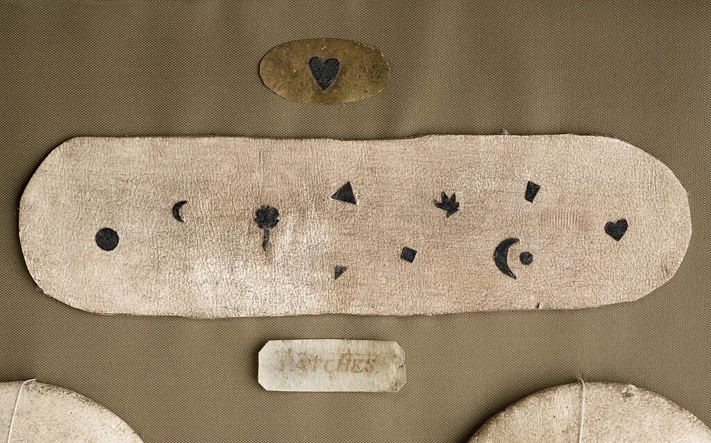 Cosmetic tools from 18th-century England, including fake beauty spots, artificial eyebrows, breast pads, and cheek enhancers once used to mask smallpox scars and follow beauty trends of the time