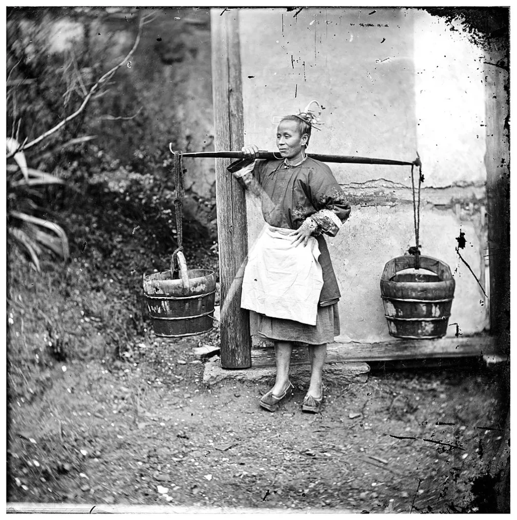 In 1871, a woman in Foochow, China carried buckets of night soil through the streets as part of her daily labor.
