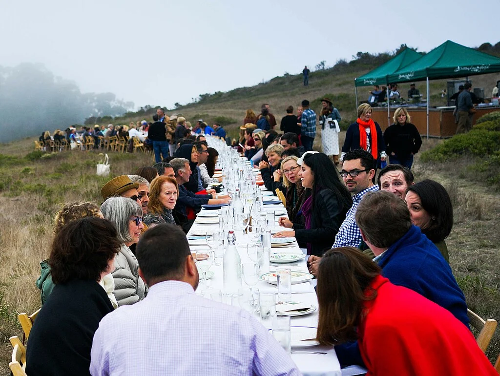 This long table setup was part of an Outstanding in the Field event in 2014, where diners gathered outdoors for a shared meal surrounded by nature.