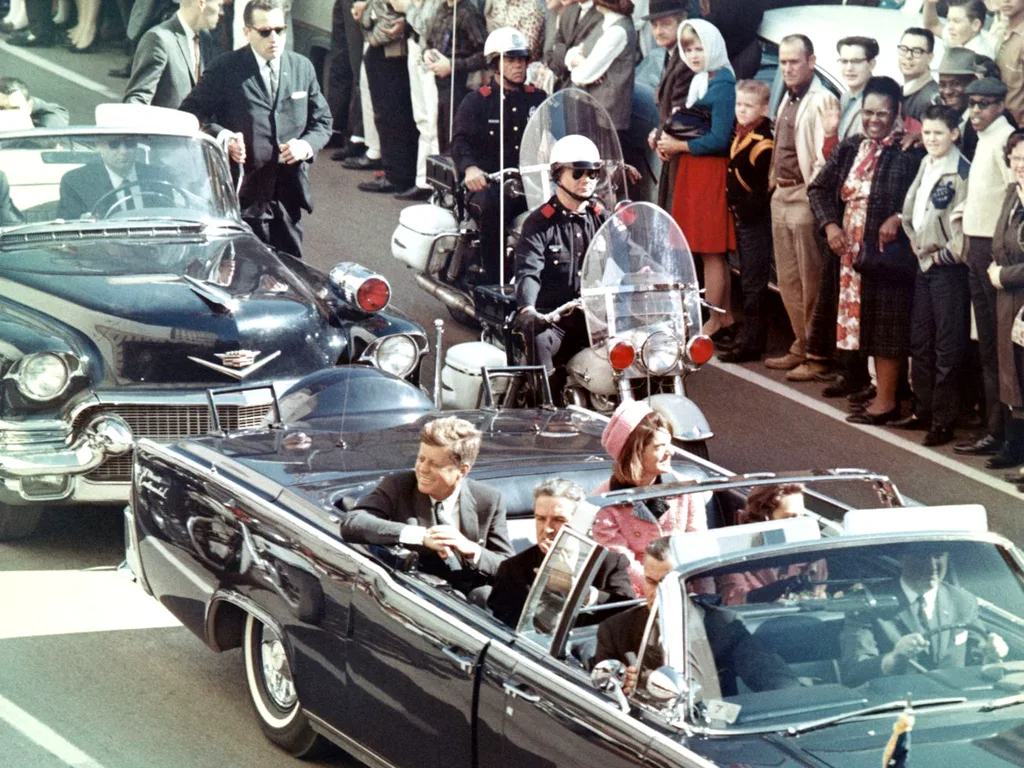 President John F. Kennedy rides through downtown Dallas on November 22, 1963, just minutes before the assassination. In the car with him are Jackie Kennedy, Texas Governor John Connally, and his wife, Nellie.
