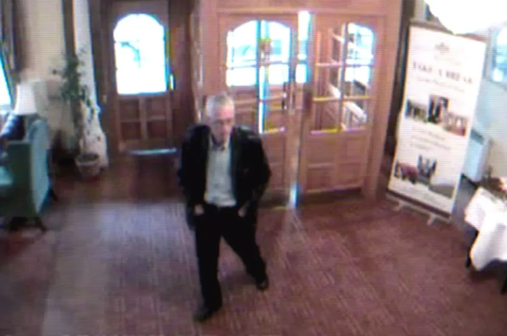 CCTV still showing the unidentified man known as “Peter Bergmann” walking through the lobby of Sligo City Hotel in June 2009, wearing a dark suit jacket and light shirt, with the hotel entrance and a display board visible behind him.