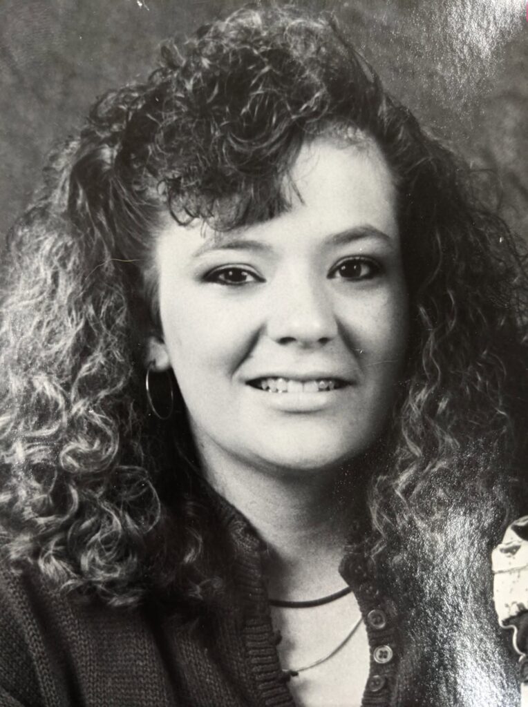 Black-and-white police-released portrait of Angela Hammond, smiling slightly with long, voluminous curly hair and hoop earrings.