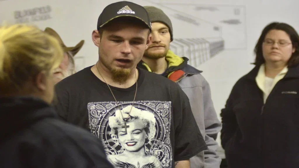 Douglas "D.J." Lockhart, wearing a black graphic t-shirt featuring Marilyn Monroe, speaks to attendees about his missing ex-girlfriend, Marina Boelter