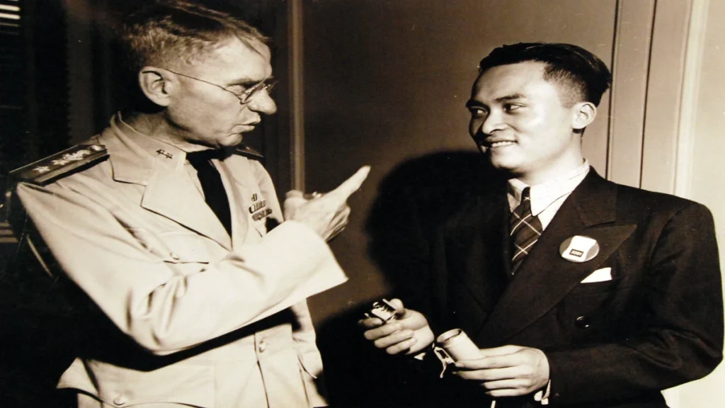 Poon Lim showing Rear Admiral Julius Furer how he made a fish hook from an electric light spring after surviving 133 days at sea.