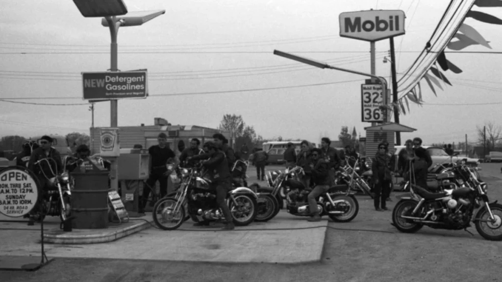 Members of the Outlaws Motorcycle Club standing beside chopper motorcycles at a Mobil service station.