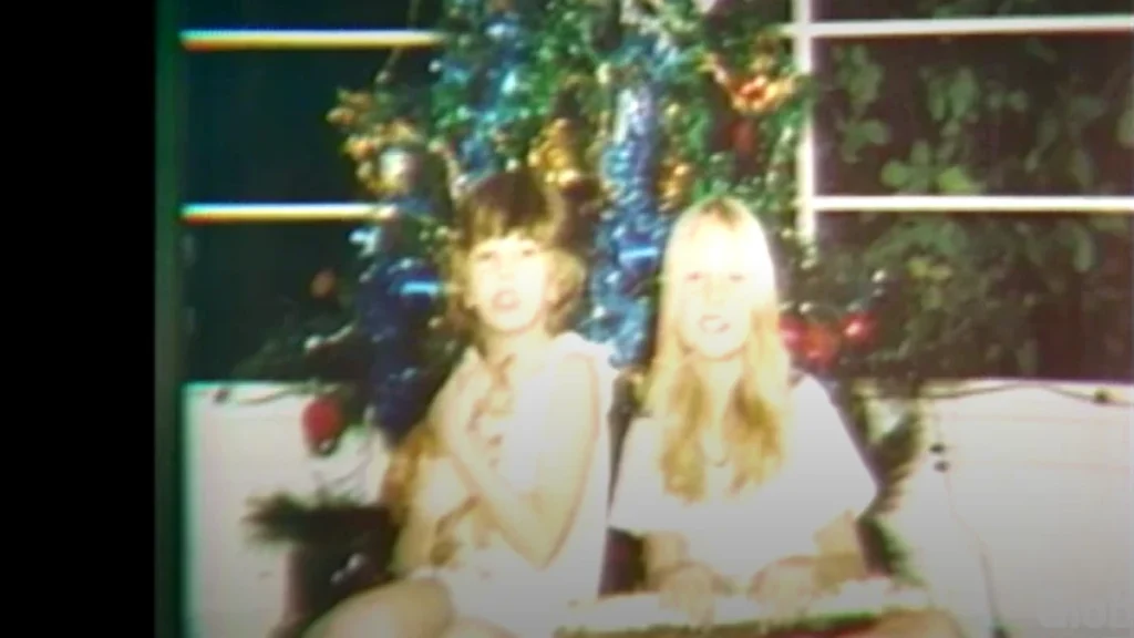 Jo-Anne Pedersen sits beside her older sister, Anna-Lise, in front of a decorated family Christmas tree.
