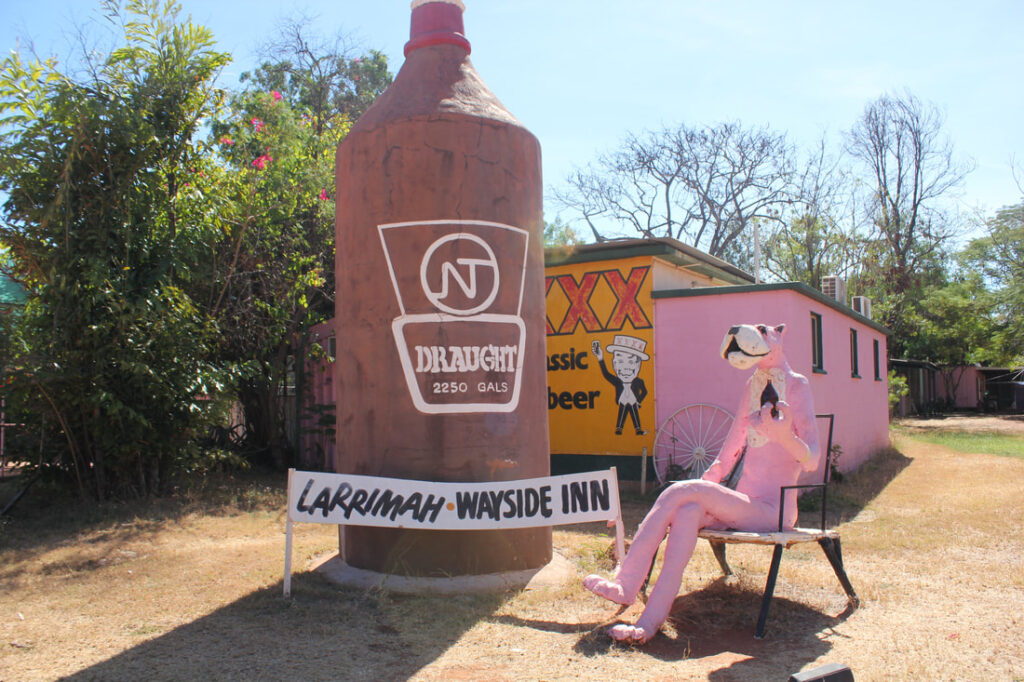A giant pink panther statue sits outside the Larrimah Wayside Inn beside an oversized vintage beer bottle sculpture in Larrimah, Northern Territory.