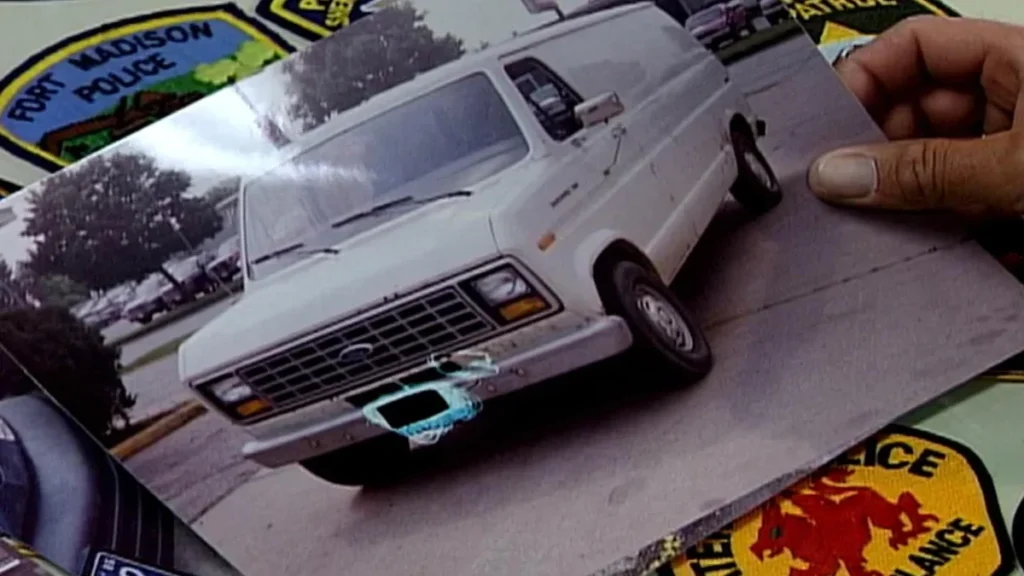 An investigator displays a photograph of a white mid-1980s Ford Econoline van matching the description of a vehicle seen at the Key Apartments