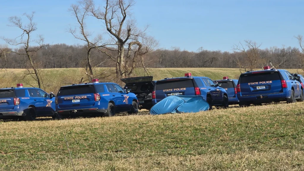 Michigan State Police vehicles beside a rural field during a search connected to Dee Warner’s disappearance.