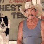 Paddy Moriarty sits at the Larrimah Hotel wearing a cowboy hat and holding a beer, beside his black-and-white dog, Rover.