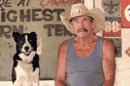 Paddy Moriarty sits at the Larrimah Hotel wearing a cowboy hat and holding a beer, beside his black-and-white dog, Rover.