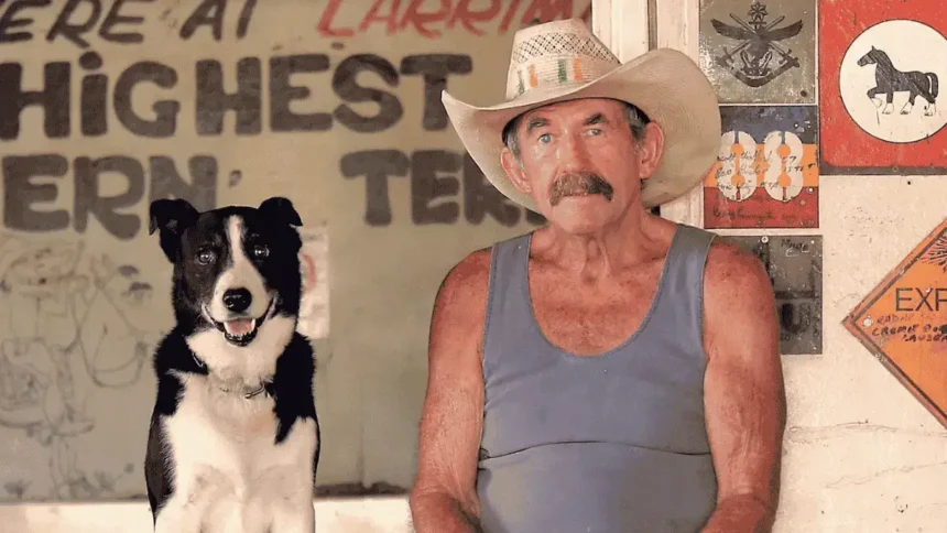 Paddy Moriarty sits at the Larrimah Hotel wearing a cowboy hat and holding a beer, beside his black-and-white dog, Rover.