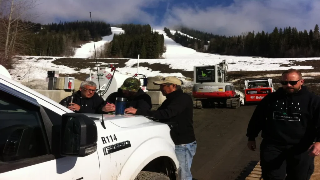 Ryan's father, Scott Shtuka (right), walking past search team members reviewing grid maps on a truck hood at the base of Sun Peaks Resort during a seasonal thaw