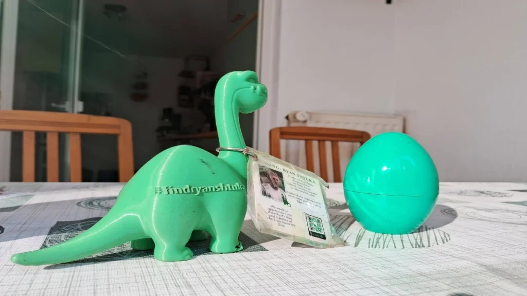 A "Shtukasaurus" 3D-printed toy dinosaur and accompanying green egg sitting on a table, carrying an information tag