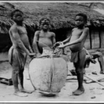 Three Congolese children stand next to a large basket used for transporting agricultural goods or trade items, circa early 1900s.