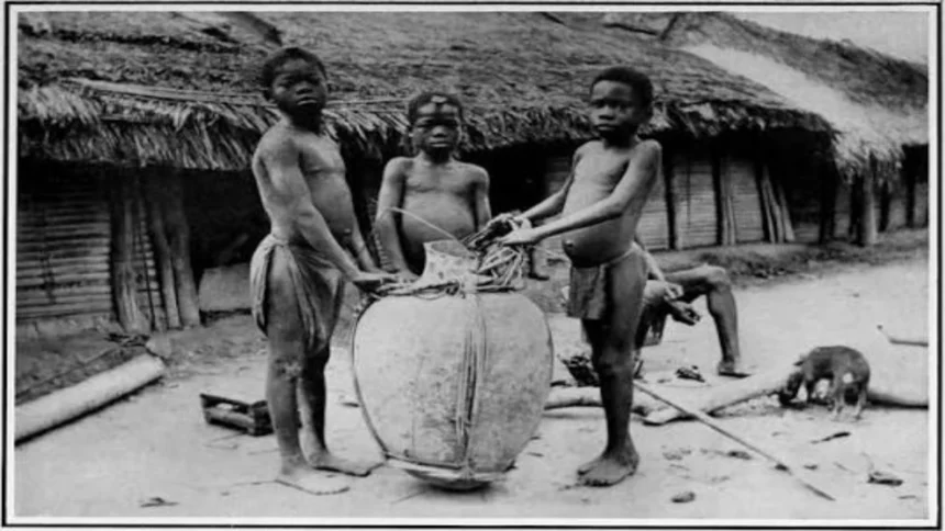 Three Congolese children stand next to a large basket used for transporting agricultural goods or trade items, circa early 1900s.