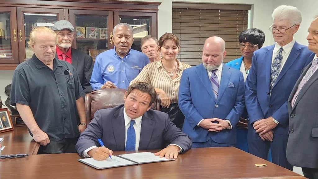 Governor Ron DeSantis signing Florida’s Dozier School victim-compensation bill with survivors and advocates present.