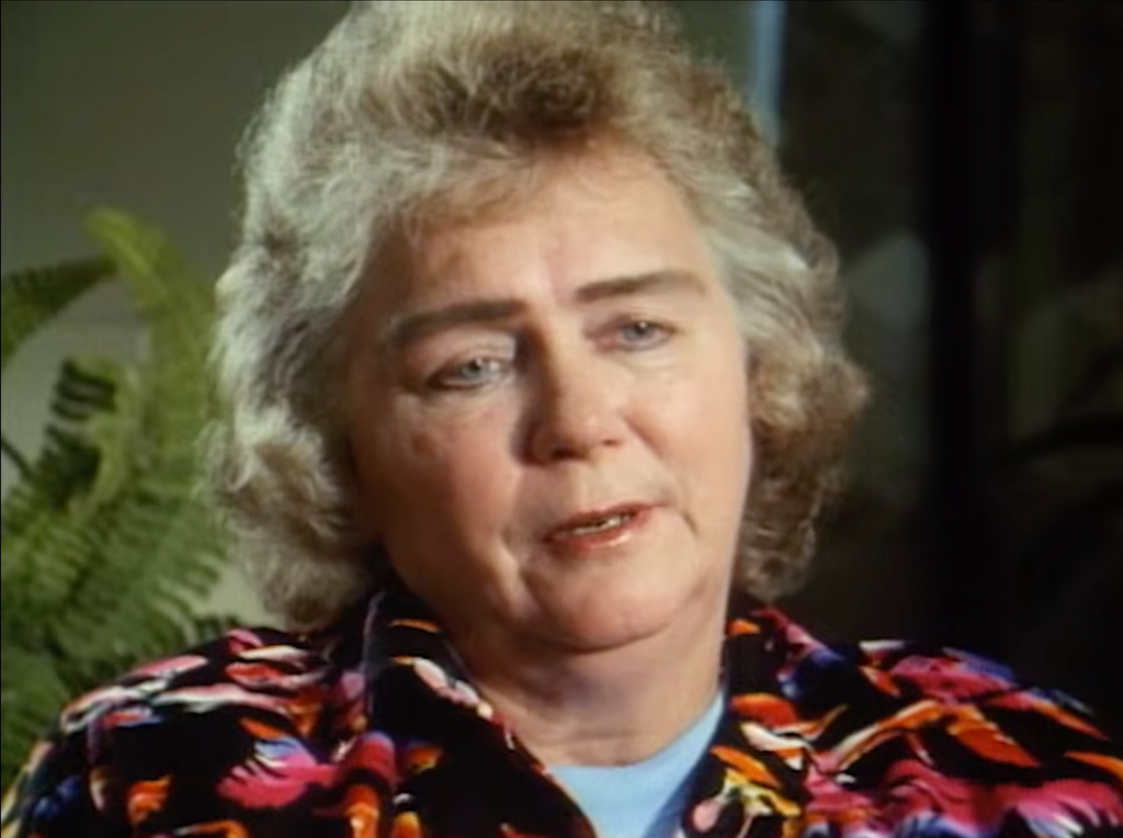 Documentary interview screengrab of Dolly Meehan, Patricia Meehan’s mother, seated indoors and speaking to camera, wearing a colourful patterned blouse.