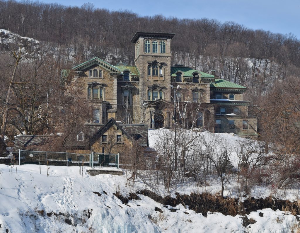 The Allan Memorial Institute’s stone façade, central tower and green roofs on a snowy slope beneath bare trees.