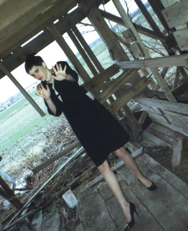 Regina Kay Walters wearing a dark dress and raising her hands inside a dilapidated wooden barn in Illinois.